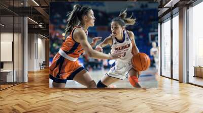 two female athletes fiercely competing in a basketball game, one dribbling the ball with focus and i Wall mural