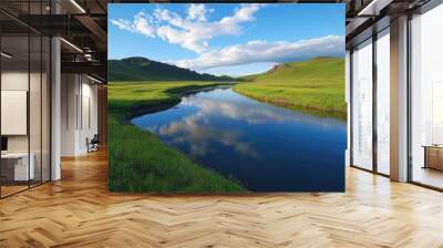 A tranquil river winding through a lush green valley, with the reflection of the sky on the water. Wall mural