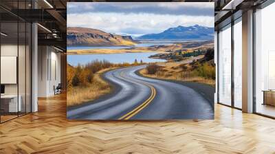 A winding asphalt road with bold road markings, disappearing into the horizon amidst Iceland's rugged scenery, with a calm lake on either side. Wall mural