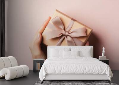 Close-up of a womans hand holding a gift box with an elegant bow, positioned against a soft-colored background, symbolizing generosity and celebration. Wall mural