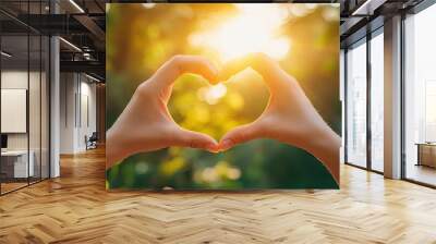 Two hands forming a heart shape against a bright sunny background, representing unity, care, and positive emotions. Wall mural