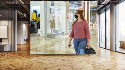 Young woman in protective mask looks at shop windows in a shopping mall Wall mural