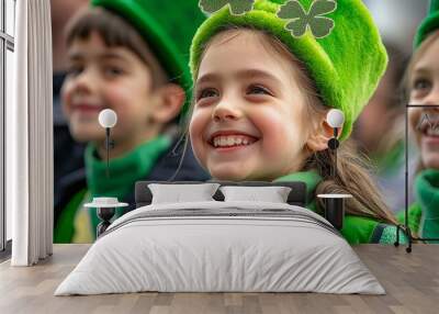 A young girl with a big smile wears a green hat with shamrocks while celebrating St. Patrick's Day. Wall mural