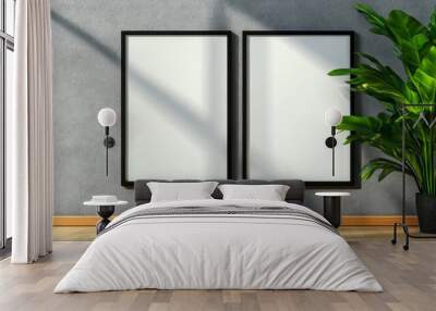 Two blank picture frames on a grey wall with a green houseplant. Perfect for showcasing artwork or photography in a modern home or office. Wall mural