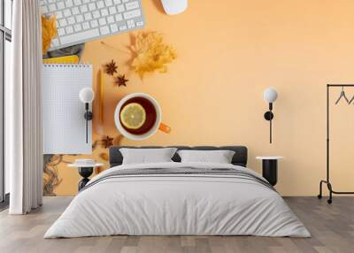 Autumn composition. Office desk with cup of hot tea with lemon, empty notebook, keyboard, scarf, dry leaves on isolated beige background. Autumn, fall business concept. Flat lay, top view, copy space Wall mural