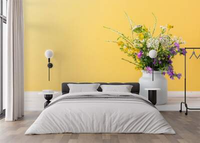 Beautiful bouquet of wild summer flowers in vase against yellow wall.  Wall mural