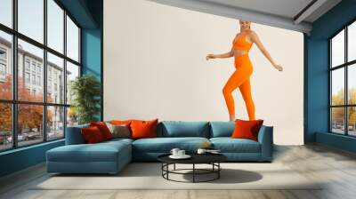 Young positive smiling woman dancing step excercise in orange fitness sport outfit cloth studio isolated shot. Wall mural