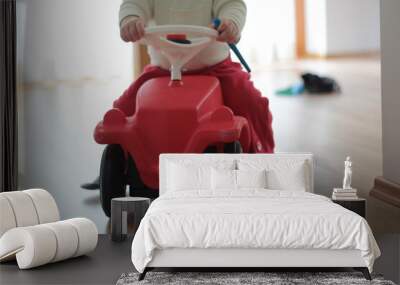 Small kid, child on a red car toy. Driving in the room alone. Wall mural