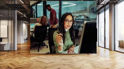 Beautiful multi-ethnic businesswoman concentrating while working on important report essay for boss sitting in office Wall mural