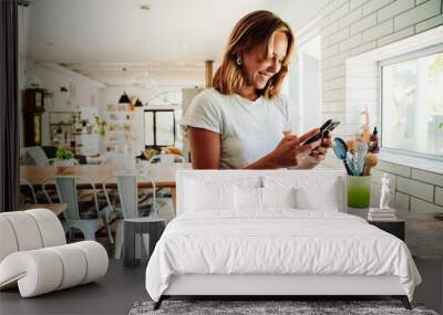 Caucasian female student working from home typing on cellular device standing in kitchen Wall mural