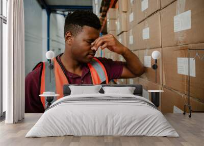 Male worker stressing after being threatened with retrenchment leaning against cardboard packages in warehouse  Wall mural