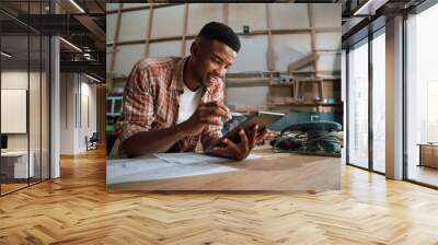 Smart African man working on tablet in wood factory Wall mural