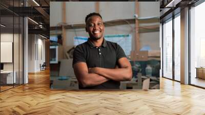 Young African man folding arms in factory Wall mural