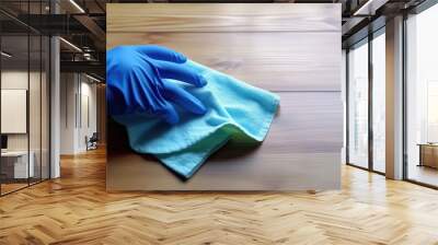 Cleaner's hand in blue rubber glove wipes wooden table top with microfiber cloth with copy space. Wall mural