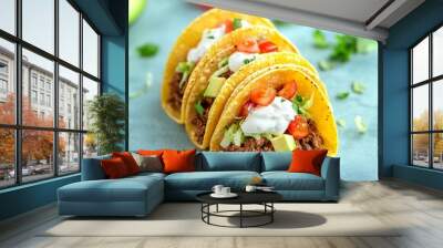 Closeup of three delicious tacos with meat, avocado, tomato, and sour cream on a blue background. Wall mural