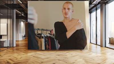 A gay guy tries on a dress in front of a mirror and throws it off Wall mural