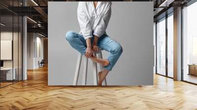 beautiful blonde woman with curly hair in jeans and a white shirt sitting on chair on studio background. Wall mural