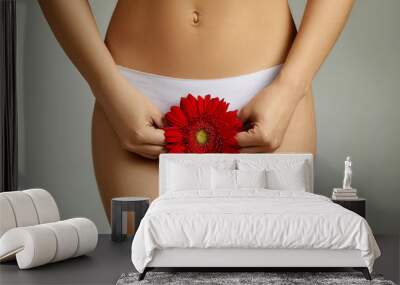 Caucasian fit woman in white underwear holding red flower on gray background. menstruation and gynecology concept Wall mural