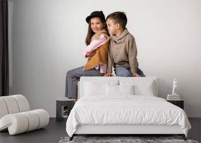 Cute stylish little couple girl and boy in fashionable clothes sittting together at studio. child boy hugs girl and tells her a funny story. kids fashion concept. Wall mural