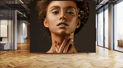 Fashion art portrait of model girl with holiday golden shiny professional makeup. beaty woman with golden sparkles on skin and hair on dark background. Gold glowing skin. Wall mural