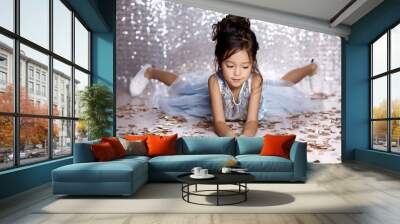 little child girl in blue dress sitting on the floor with confetti on background with silver bokeh. birtday party Wall mural