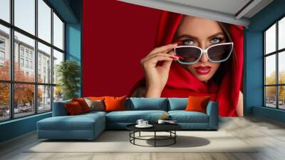 Portrait of beautiful brunette sexy girl with luxurious make-up in white sunglasses and red headscarf on red background. woman look at the camera Wall mural