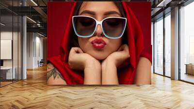 Portrait of beautiful brunette sexy girl with luxurious make-up in white sunglasses and red headscarf on red background Wall mural