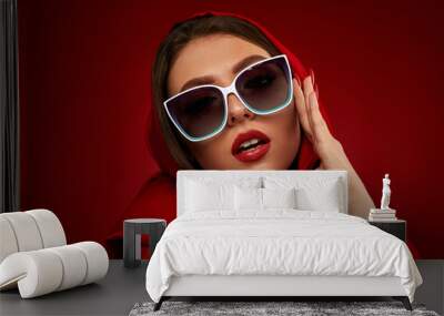 Portrait of chic brunette sexy girl with luxurious make-up in white sunglasses and red headscarf on red background Wall mural