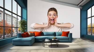 Portrait of young surprised beautiful woman screaming with shocked facial expression on gray background Wall mural