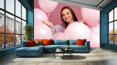 Smiling pleased girl posing with pastel pink air balloons on pink background. Beautiful happy young woman on a birthday holiday. close-up Wall mural