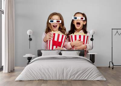 two beautiful surprised caucasian little girls in red-blue 3d glasses holding popcorn buckets and watching movie Wall mural