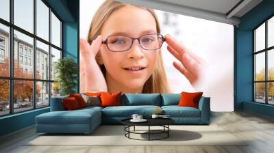 Young little girl trying glasses at the optician Wall mural