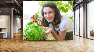 Young woman taking care of her plants and vegetables on her city balcony garden - Environment and ecology theme Wall mural