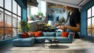 a woman cooking in a kitchen with a skillet and vegetables on the stove top Wall mural