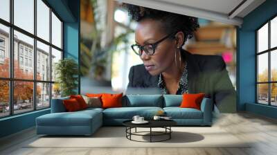 a woman wearing glasses looking at a laptop computer screen while sitting at a table Wall mural