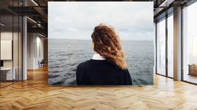 Rear view of young woman looking at overcast sky and gray sea Wall mural