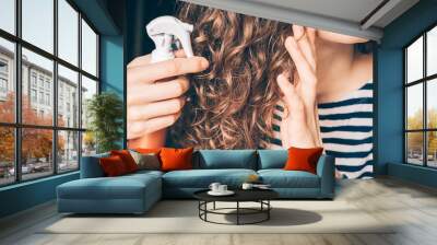 Woman applying spray on curly brown hair Wall mural