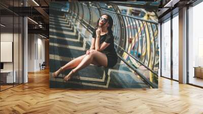 Beautiful fashionable girl in black clothes and sunglasses walking around the city.  Wall mural