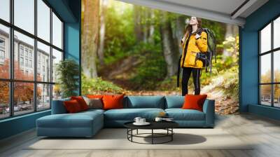 cheerful brunette tourist girl wears orange jacket and backpacked have walk through forest, autumn t Wall mural