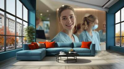 A smiling nurse stands in front of three other nurses at a hospital reception desk. Wall mural