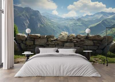 A stone wall sits in a grassy area in front of a mountain range. The sky is blue with white clouds. Wall mural