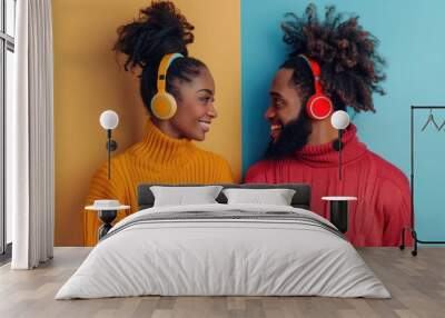 Young African American couple with headphones exchanging warm smiles against yellow and blue background, reflecting a romantic and joyful interaction. Wall mural