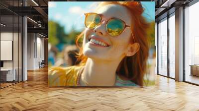 Young woman with red hair and freckles wearing yellow sunglasses smiling and looking up on sunny day in park. Wall mural