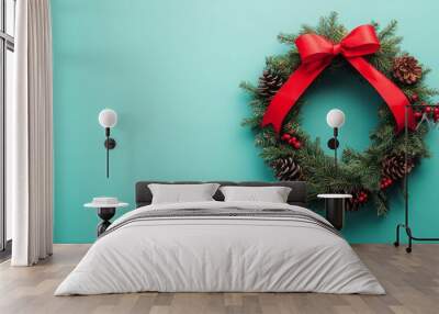 A beautifully crafted green wreath decorated with a bright red bow and pinecones rests against a vivid turquoise backdrop, creating a cheerful holiday ambiance suitable for seasonal celebrations. Wall mural