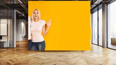 A cheerful family stands side by side, smiling widely with their arms raised in a wave. The vibrant yellow backdrop enhances their joyful expressions, capturing a moment of togetherness and happiness. Wall mural