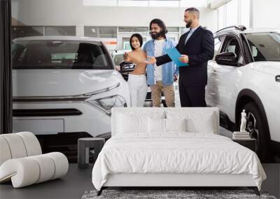 A couple of individuals are standing in front of a row of parked cars. The people appear to be conversing or taking a break. The cars are neatly lined up in the background. Wall mural