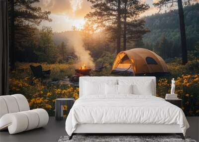 A cozy camping setting unfolds as a yellow tent stands by a fire surrounded by blooming wildflowers. The sun sets behind tall trees, casting a warm glow over nature. Wall mural