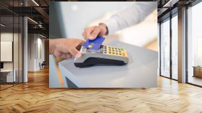 A customer is making a contactless payment by tapping a card on a payment terminal at a retail checkout. The cashier assists with the transaction in a bright store environment. Wall mural