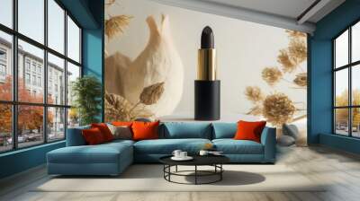 A dark lipstick stands prominently on a round pedestal surrounded by smooth stones and dried floral arrangements, showcasing a minimalist aesthetic with a touch of natural beauty. Wall mural