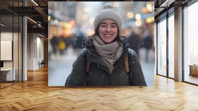 A joyful woman stands in the midst of a snowy street, surrounded by festive lights and bustling shoppers. She's bundled up in a warm coat and hat, expressing happiness during the winter season. Wall mural